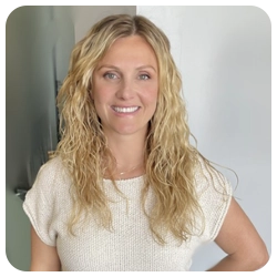 Woman with blond curly hair, smiling at camera in white shirt.