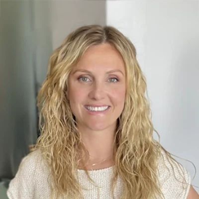 Woman with blond curly hair, smiling at camera in white shirt.